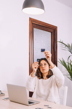 Young female photographer sitting at table with laptop and photo camera with projector and working with old photo slides at home workplace