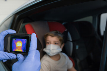 Crop doctor in medical gloves measuring temperature of boy while using infrared camera during coronavirus epidemic