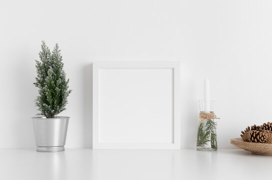 White square frame mockup with a cypress tree, candles and pine cones on a white table. Christmas decoration.