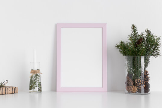 Pink frame mockup with a bouquet of fir, candle and a gift on a white table. Christmas decoration.