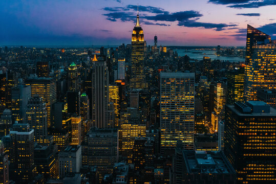 Aerial view of megalopolis with illuminated glass walls and futuristic facades of tall skylines on background of majestic sunset