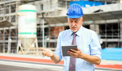 Senior engineer man in suit and helmet working on tablet pc in a skeptics expression