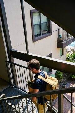 From above back view of male with paper bags and backpack walking upstairs in modern building