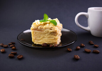 Piece of layered cake on a saucer with spoon and cup on background. Russian cake Napoleon on dark background. Birthday cake.
