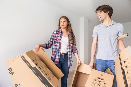 Young couple moving carton boxes in new empty apartment with opened door