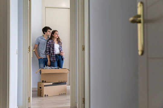 Young couple moving carton boxes in new empty apartment with opened door