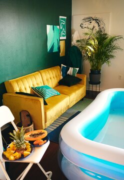 High angle of creative apartment with inflatable pool for home party and fresh tropical fruits placed on chair