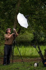 Mature male photographer gray beard glasses floppy hat brown shirt outside in green wooded area...
