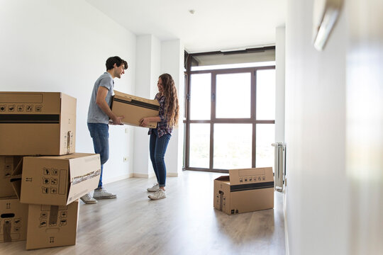 Young couple unpacking in empty apartment with many carton boxes