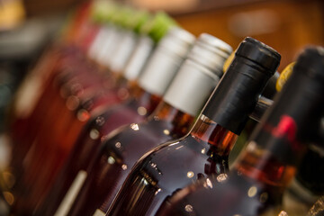 Close-up of filled bottles of red wine unopened and composed in row on shelf in bar.