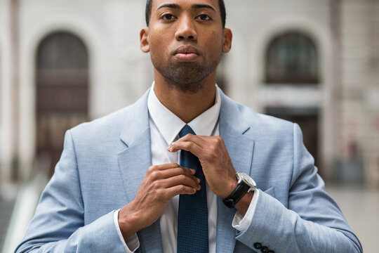 Close-up portrait of handsome serious African-American man in trendy blue suit rearranging tie