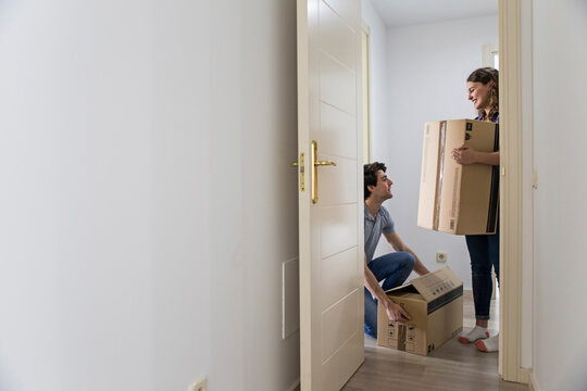 Young couple moving carton boxes in new empty apartment with opened door