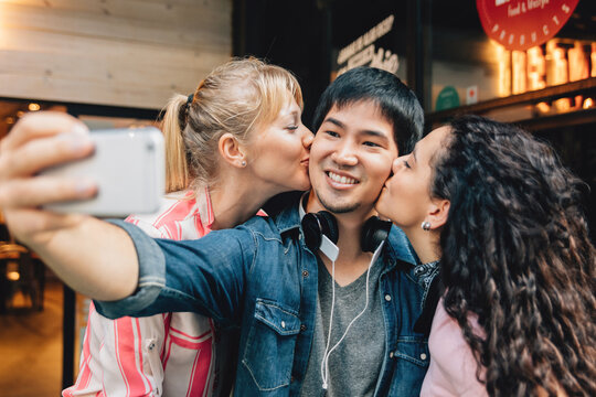 Girls kissing a young man taking a selfie