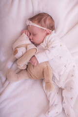 Cute little baby sleeping in white pajama with teddy bear toy. Portrait of small cute girl in her cozy white bed.
