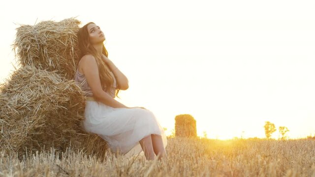 beautiful girl sitting lean on a haystack in field at sunset,young woman in skirt enjoying nature