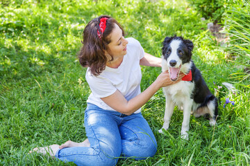 Smiling young attractive woman playing with cute puppy dog border collie in summer garden or city park outdoor background. Girl training trick with dog friend. Pet care and animals concept.