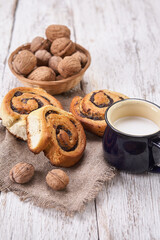 Basket of homemade buns with jam, served on old wooden table with walnuts and cup of milk