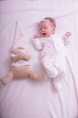 Portrait of a child on a white background with plush bear toy. Baby girl 1 months among toys. Space for text.