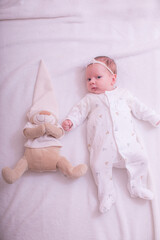 Portrait of sleeping one month old newborn baby girl laying with teddy bear. Flat lay composition. Cute baby girl on a light background in bed. At home.