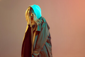 Cool stylish young girl, posing in hoodie and cloak with developing hair on a neon beige background.