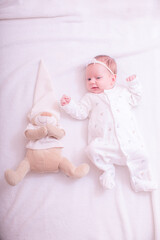 Cute baby girl on a light background in bed at home with teddy. Close up portrait of infant baby 1 months old. Image in pink rose gold color.