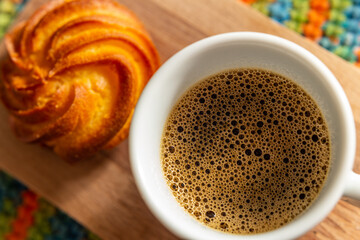 Detalhe de café com espuma em xícara branca e broa de milho.