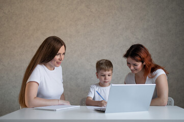 Fototapeta na wymiar Happy same-sex lesbian family with a child stays at home. Two mothers help the boy do school homework. A couple of women help their son with distance learning. Quarantine.