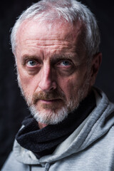 Middle aged man with blue eyes, short gray messy hair and beard wearing hoodie and neck gaiter,...