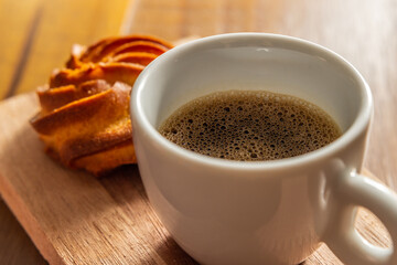 Close em café com espuma em xícara branca e broa de milho em mesa de madeira.