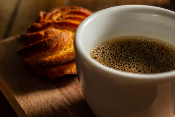 Close em café com espuma em xícara branca e broa.