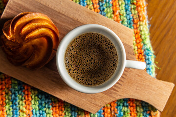 Café em xícara de cerâmica sobre mesa com forro de crochê colorido.