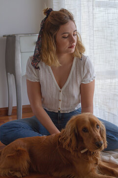 Chica joven sentada en el suelo de madera de su habitación junto a su perro mirando por la ventana