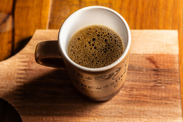 Xícara com café, com espuma, sobre uma mesa de madeira.