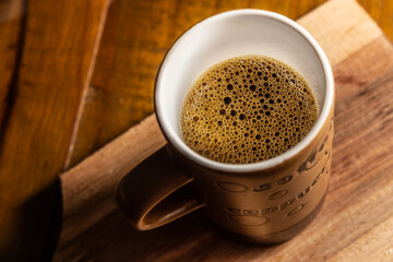 Xícara cheia de café sobre uma mesa de madeira.