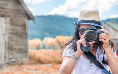 Woman wearing straw hat making pictures of mountain landscpae with wooden hut