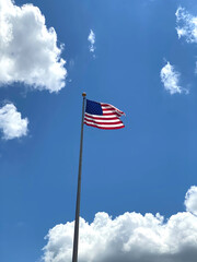 American flag flying with clouds and brilliant blue sky.