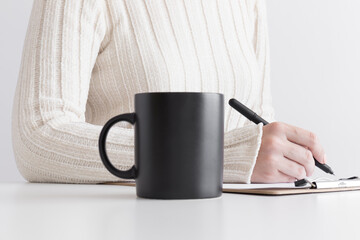 Black mug mockup with woman taking notes on a clipboard.