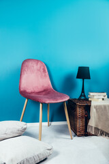 Modern Pink Velour Chair with Beige Cushion, Wicker Chest with Lamp as Eiffel Tower and Cashmere Throw nearby. Modern interior in the house. Blue wall as background