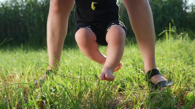 baby boy does first steps grass happy family. mom helps baby son take steps with his feet. people in the park dream kid concept happy family childhood. child son walks barefoot on lifestyle green