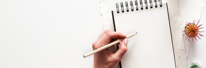 Sketchbook on a white background and a female hand with a pencil. Mockup. Panorama.