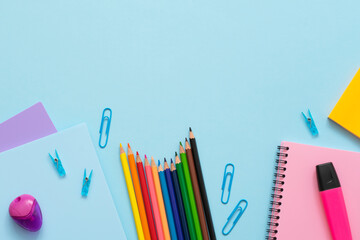 School supplies on the blue background. Top view of blue, purple and pink notebooks, color pencils, watercolor, paper clips, markers and eraser. Education concept.