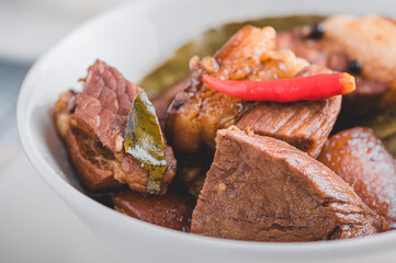 Pork Adobo (focused) is a Filipino dish stewed in vinegar, garlic, onion,  soy sauce, bay leaves, peppercorns .