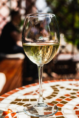A glass of white wine on a mosaic stone table of a cafe terrace on a sunny day