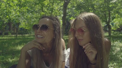 Naklejka premium Two beautiful young women in sunglasses are lie on green grass