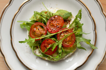 Overhead view of cherry tomato and rocket salad on top of round grain toast on white plate. Healthy eating concept.