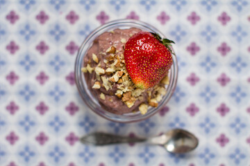 Top view on a fruit dessert with a big strawberry and chopped nuts on top and a spoon on background