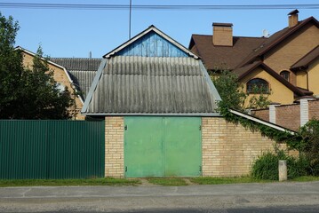 Fototapeta na wymiar brown brick garage with green iron gates under a gray slate roof on a rural street