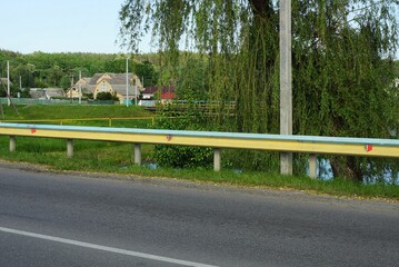 yellow long iron barrier  off an asphalt road against green vegetation a blue sky