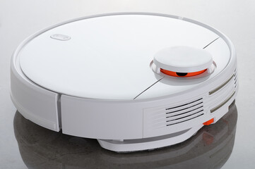 White robot vacuum cleaner with wet cleaning function, against the background of mirrored gray granite very close-up.