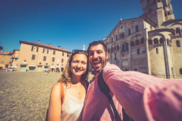 Fototapeta na wymiar happy Tourist couple visit city center of Modena in the main square of the city taking selfie photo together. Major destination in Emilia-Romagna, Italy